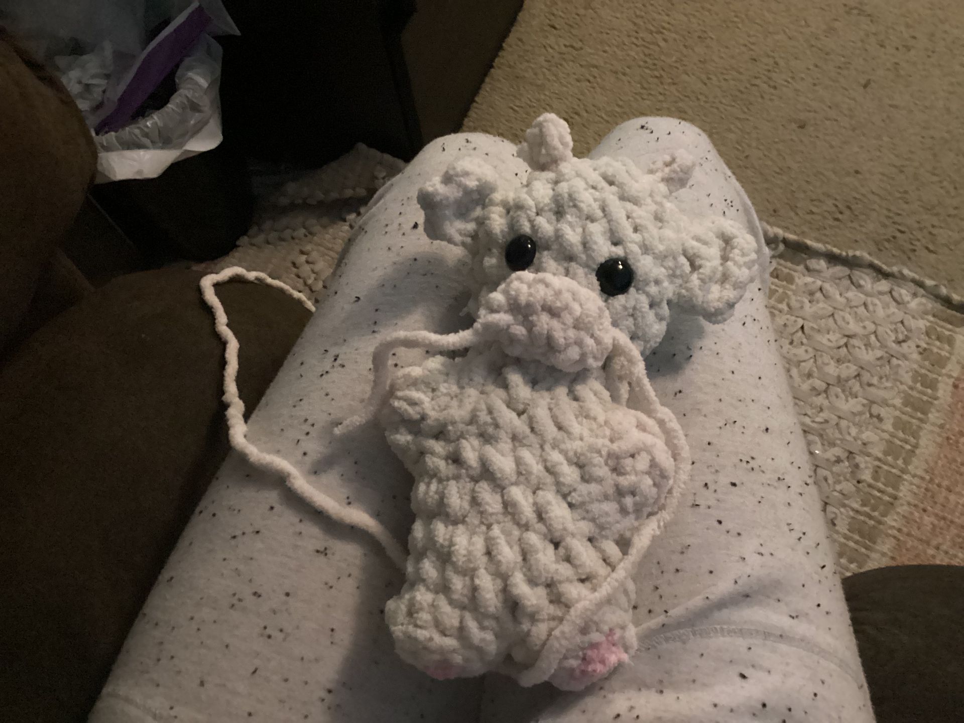 White crocheted plush animal with black eyes resting on a white speckled pillow on a couch