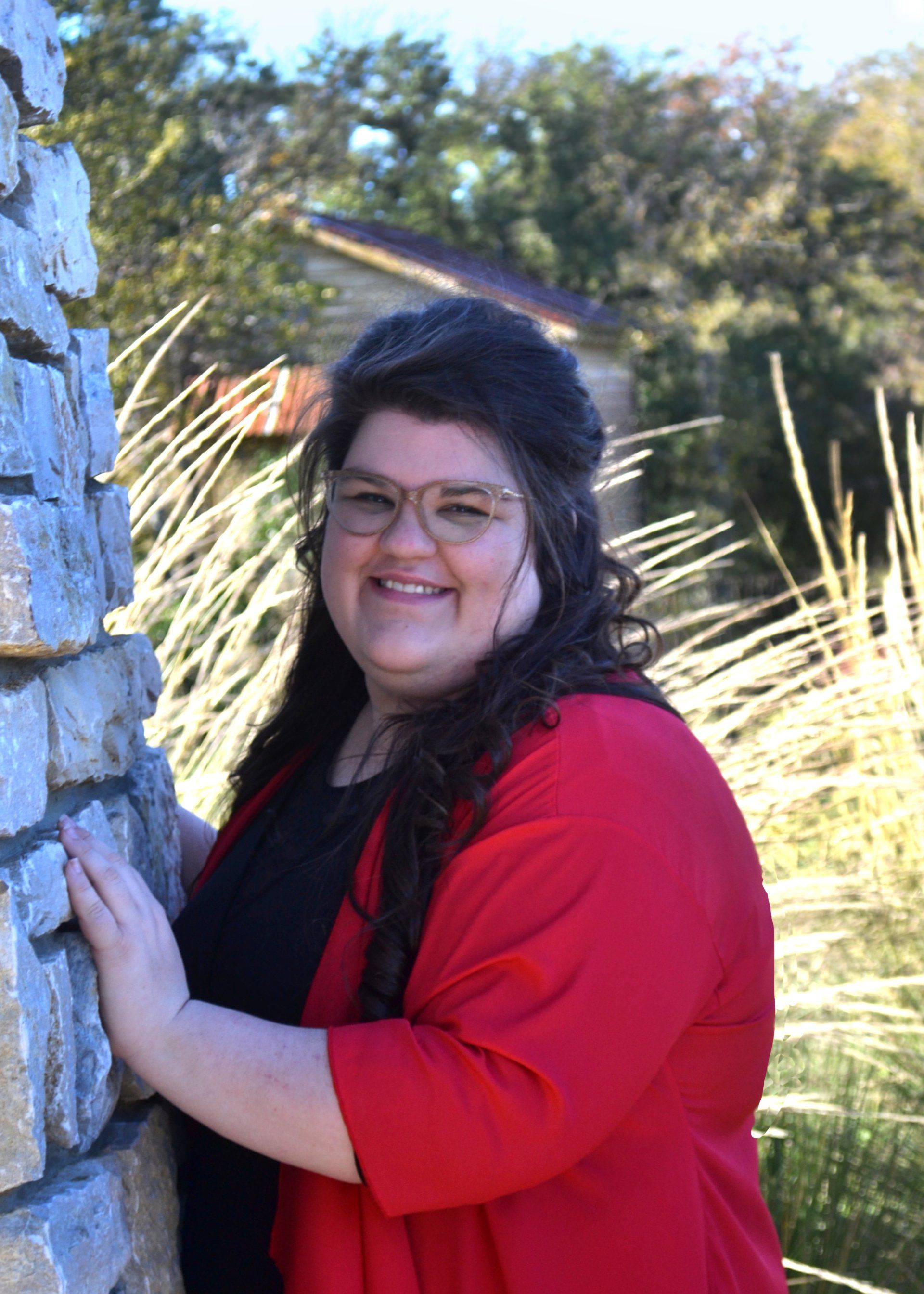 A woman in a red jacket is leaning against a stone wall.