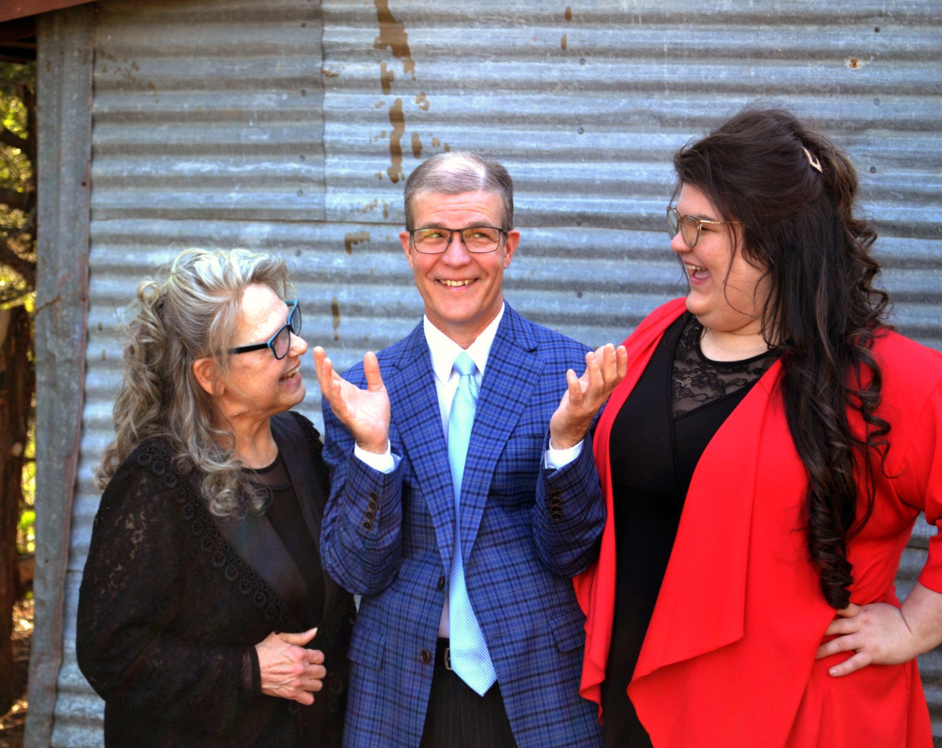 A man and two women are standing next to each other in front of a tin shed.