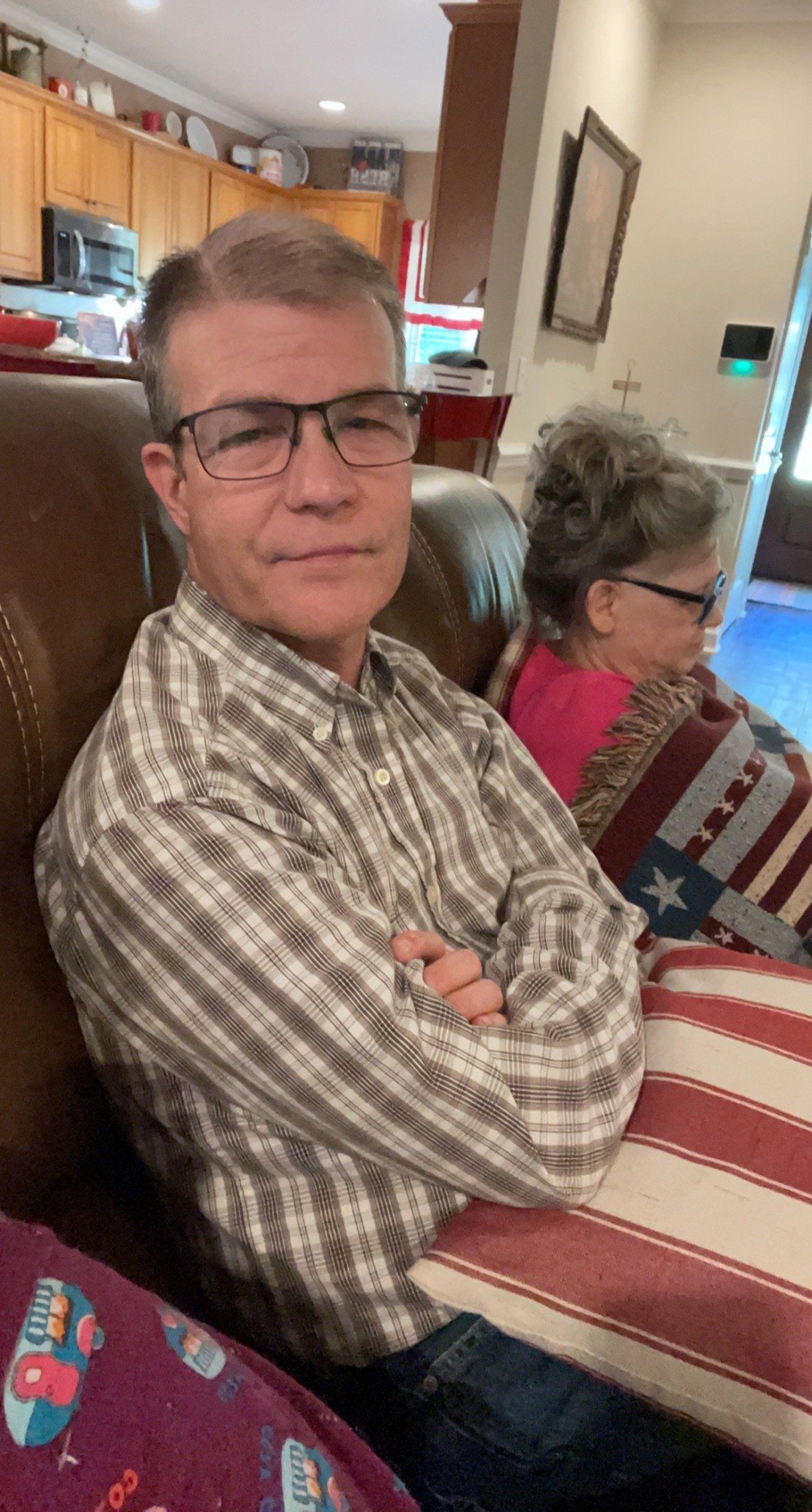 A man wearing glasses is sitting in a chair with his arms crossed.