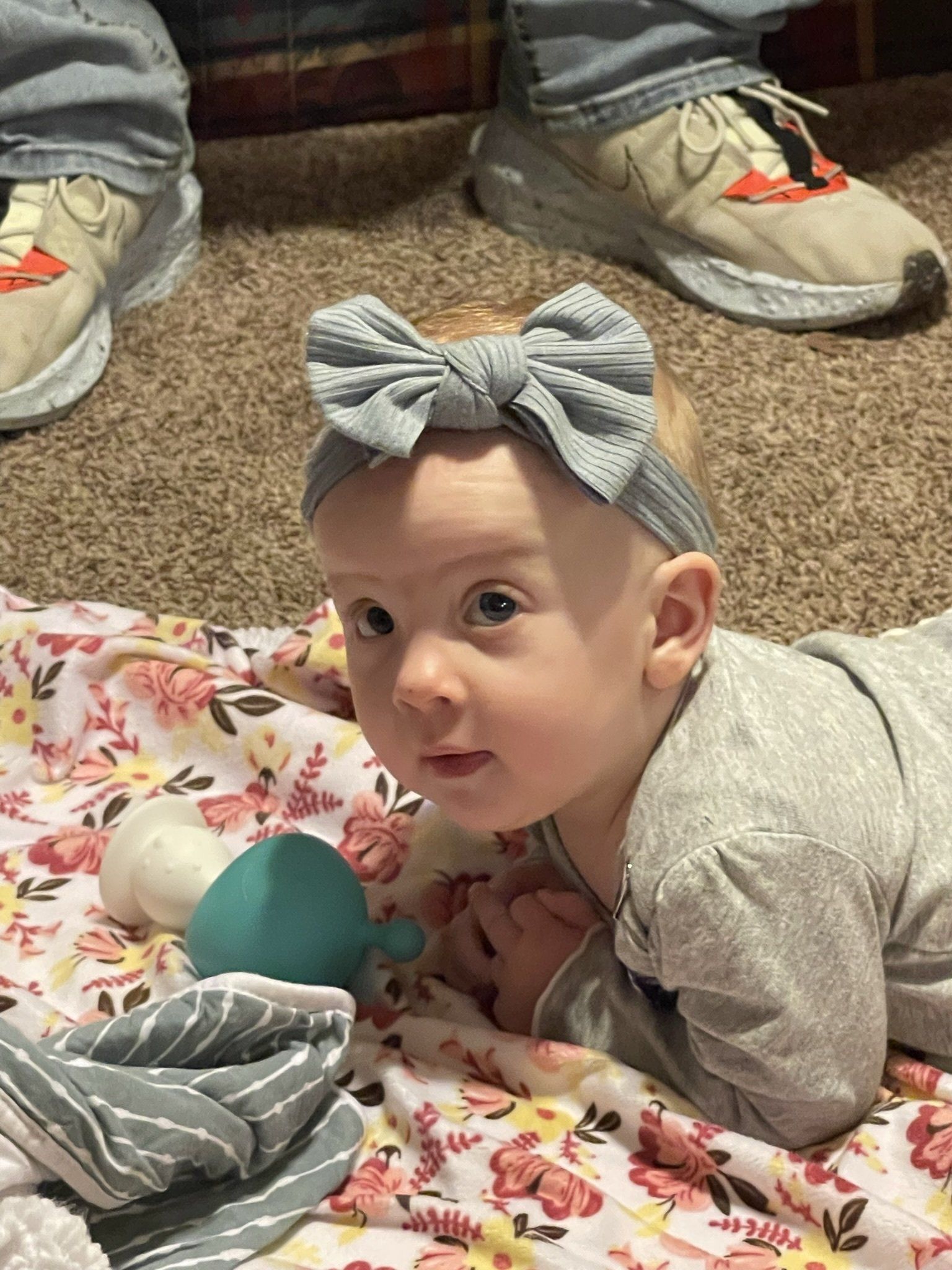 A baby with a bow on her head is laying on a blanket.