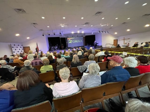 A large group of people are sitting in chairs in front of a screen that says omaa