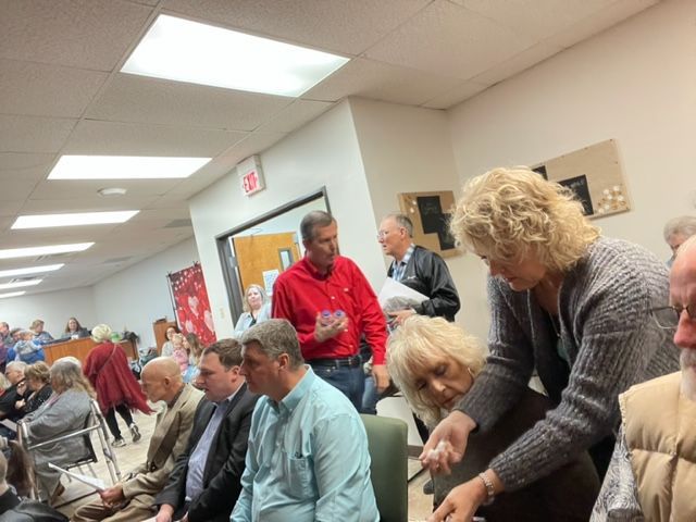 A group of people are sitting in a room with a fire exit sign on the wall