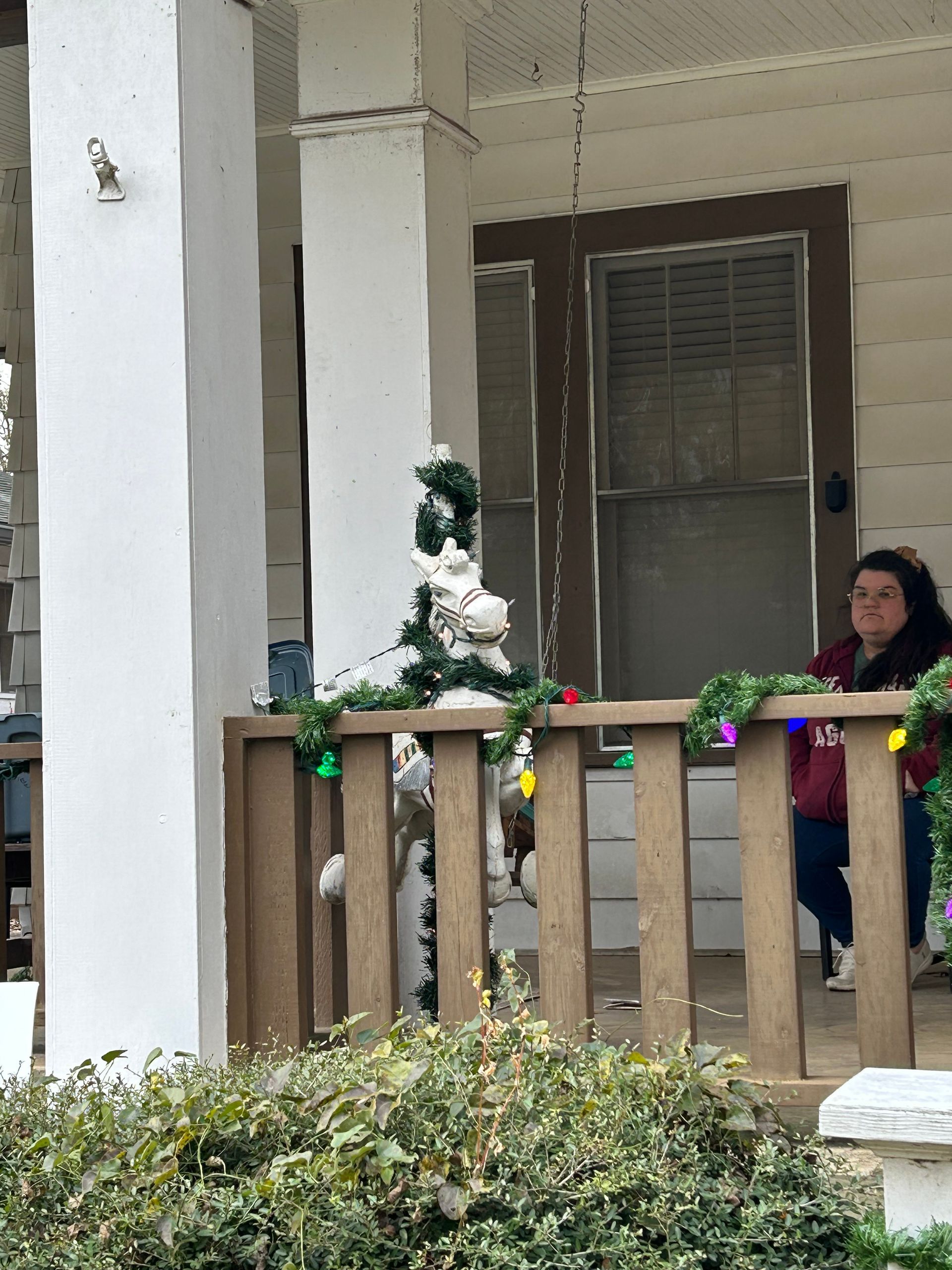 Woman on porch with Christmas decorations, including a garland and small tree.