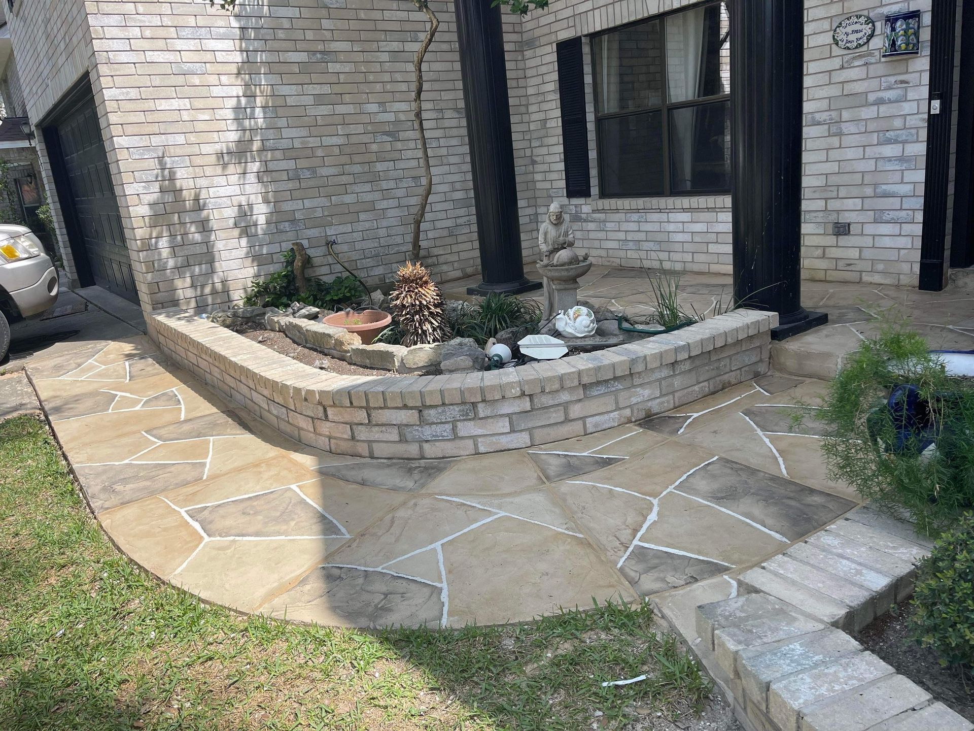 Stone pathway curving toward a brick-walled garden bed in front of a light brick house.