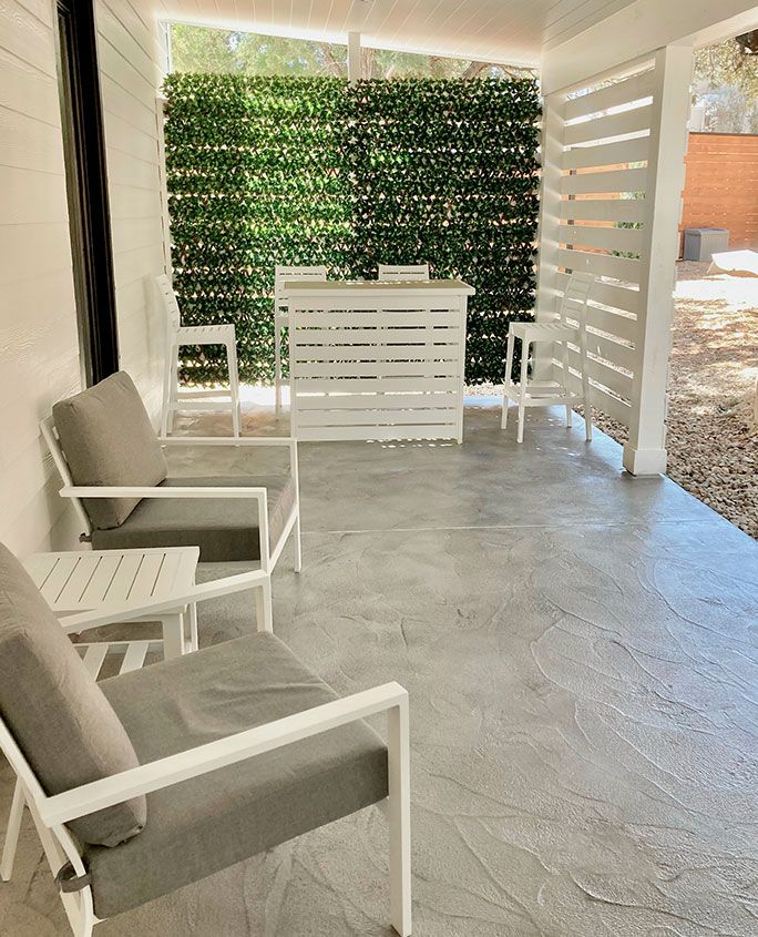 Outdoor patio with white furniture, bar, and green wall.