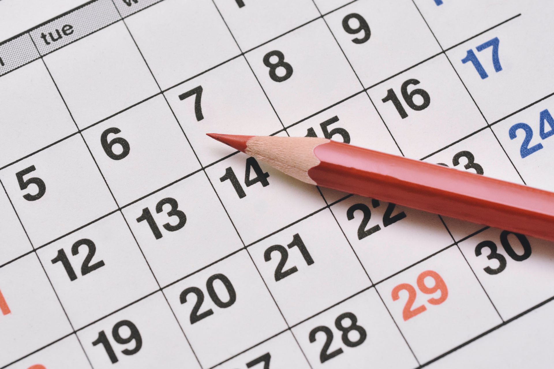 Red pencil pointing at a date on a wall calendar.