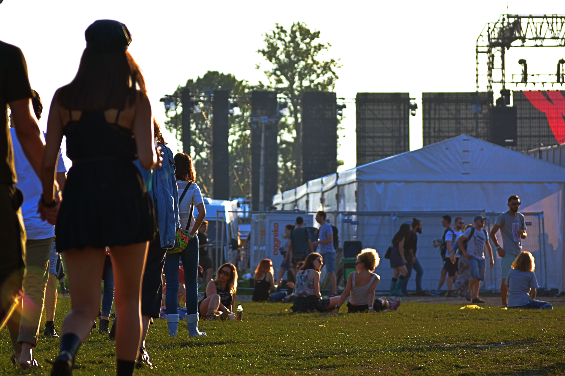 People gathered on a grassy field near white tents and tall structures at an outdoor event.