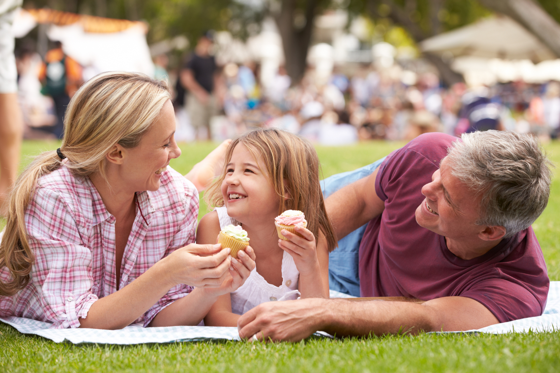Three people lying on grass, smiling and eating ice cream in a park