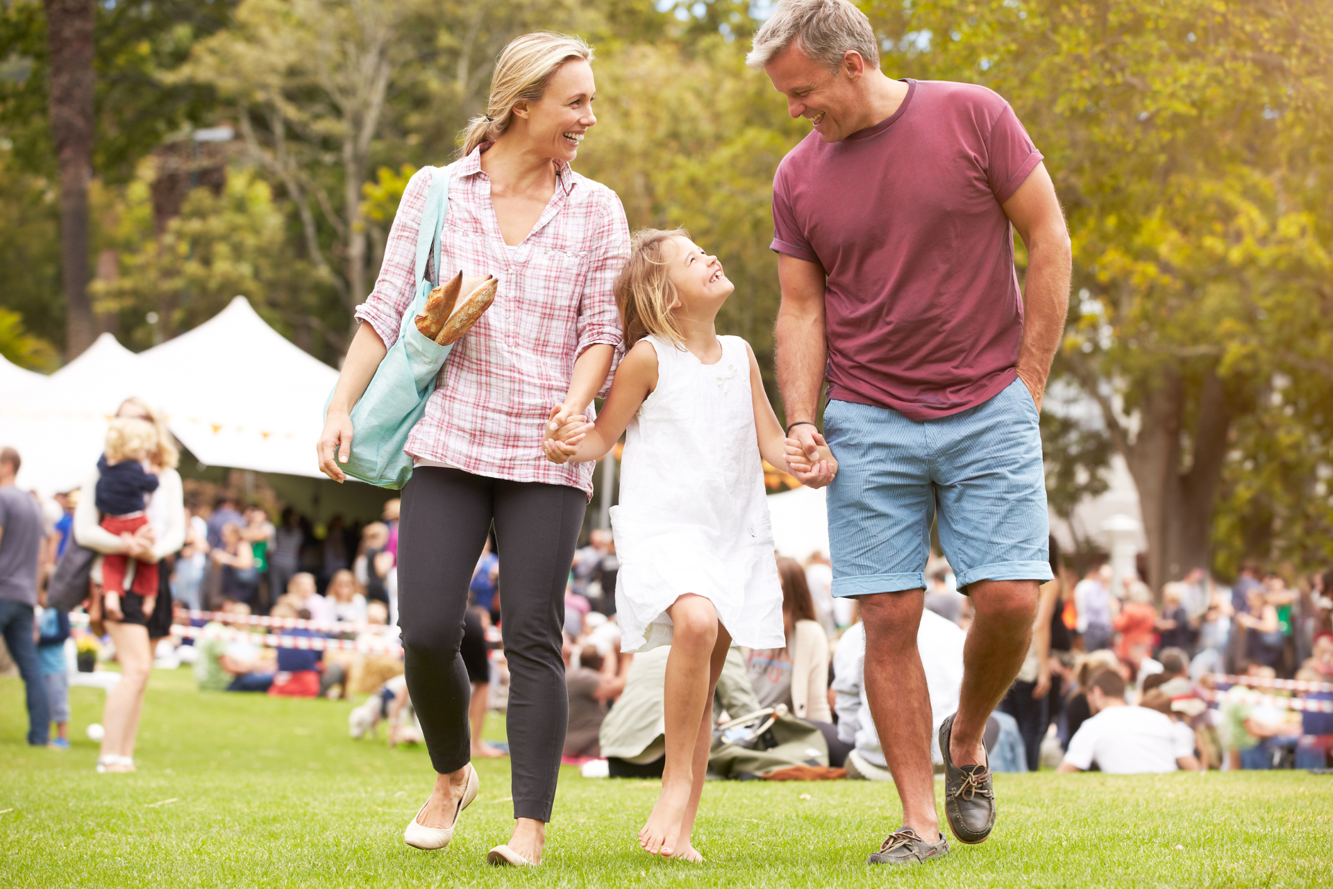 Family walking on grass at an outdoor fair, with white tents and people in the background.