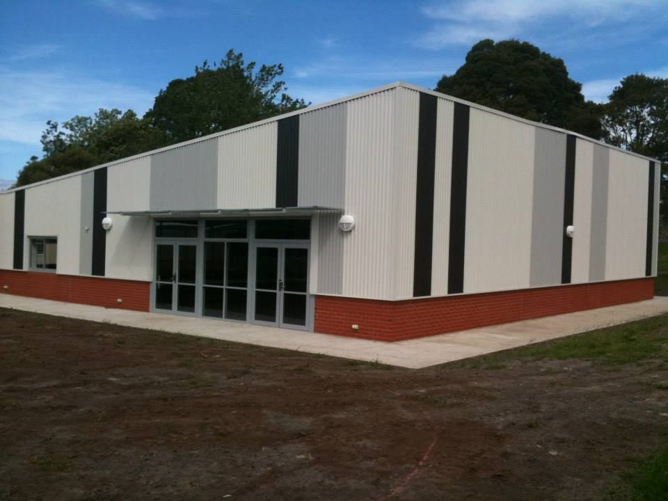 Modern single-story building with white, grey, and black vertical panels, a red brick base, and glass entrance doors.