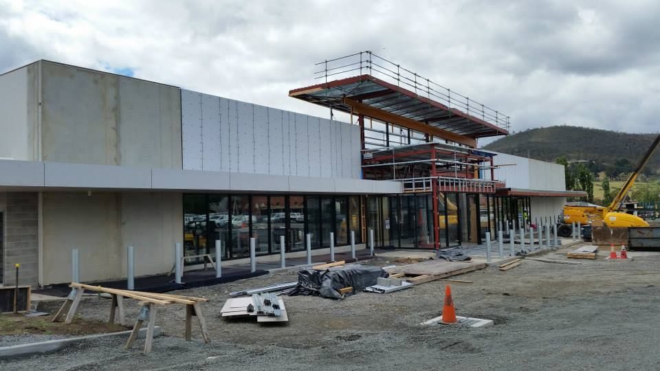 A construction site featuring a modern, partially finished building with white paneling, glass doors, and metal scaffolding.