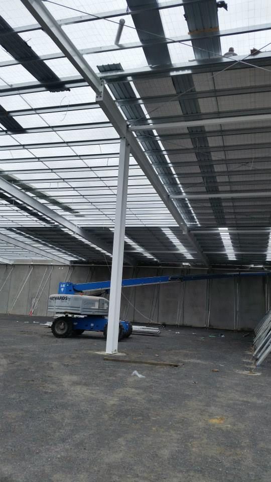 A blue articulated boom lift parked inside an unfinished industrial building with a steel frame ceiling.