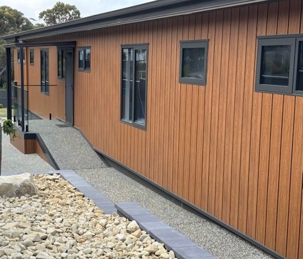 Modern building exterior with wood siding, narrow windows, and a gravel accessibility ramp leading to the entrance