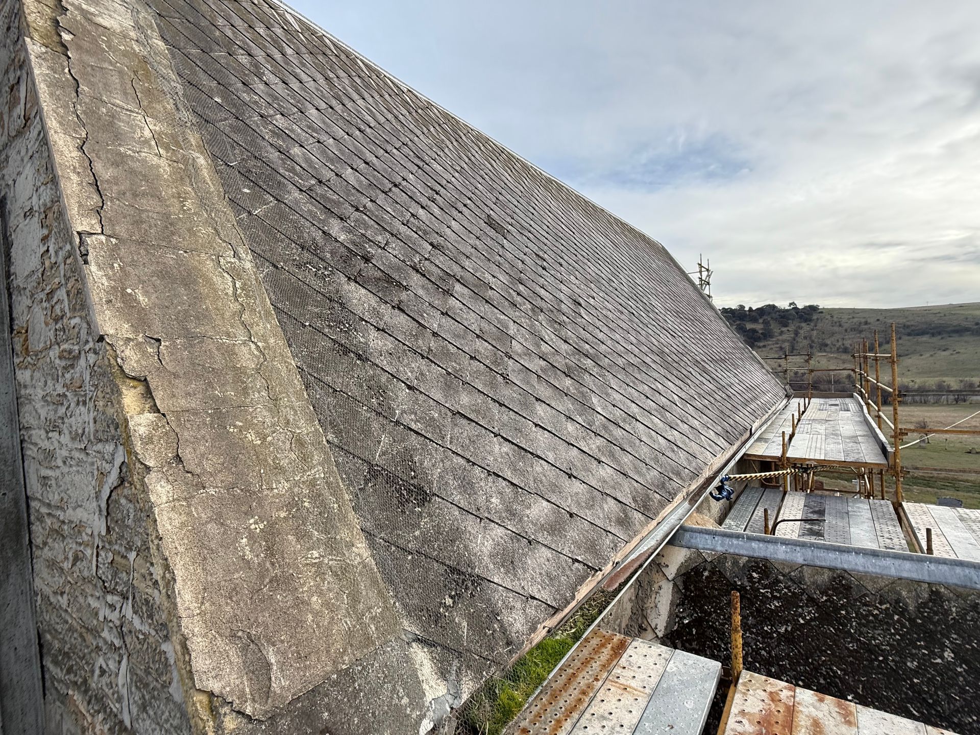 A stack of weathered, grey, corrugated asbestos cement roof panels lying outdoors.