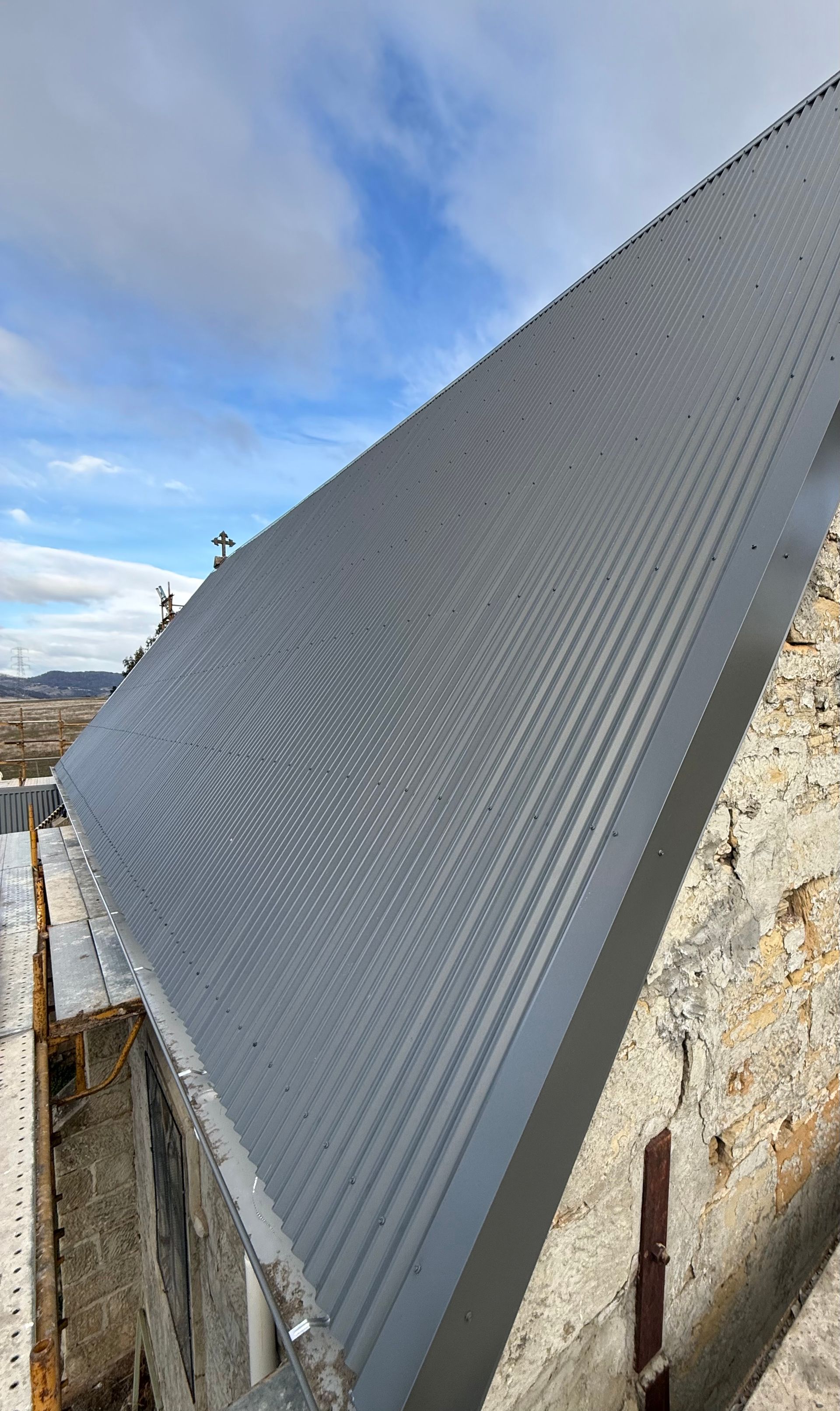 Gray corrugated metal roof panel leaning against a weathered rooftop wall under a blue sky