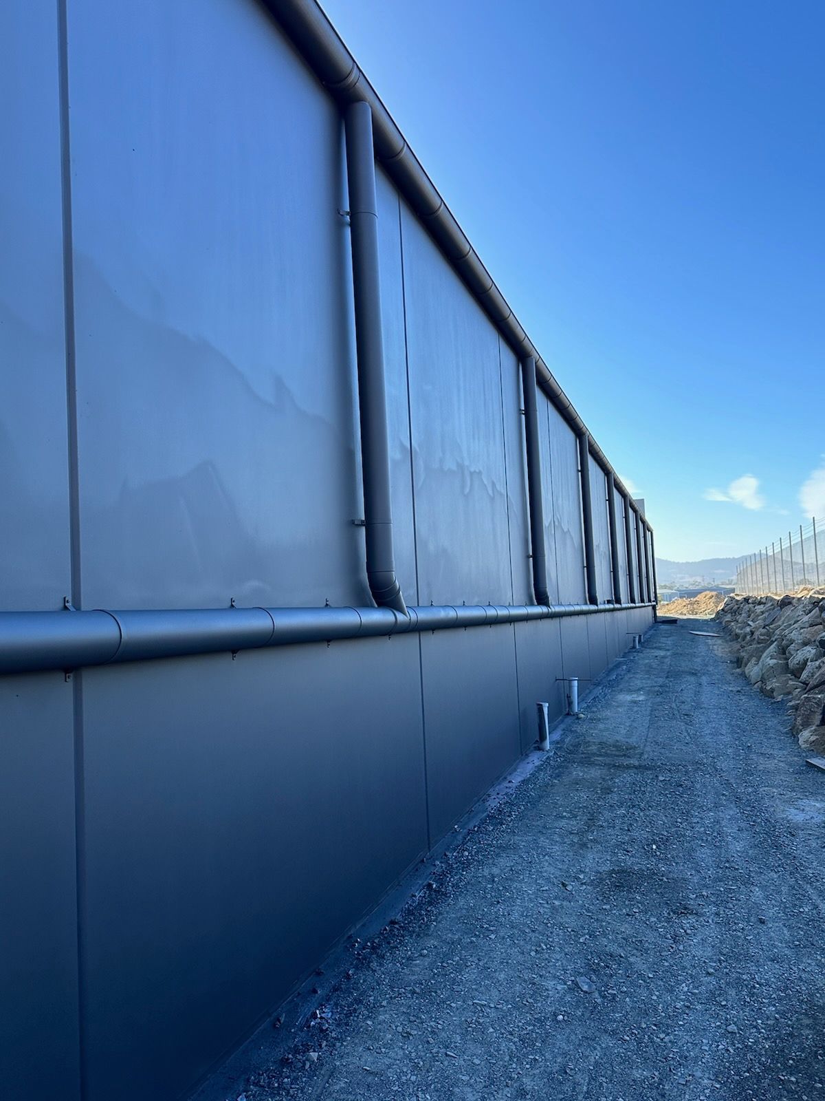 Blue metal wall beside a gravel path under a clear sky