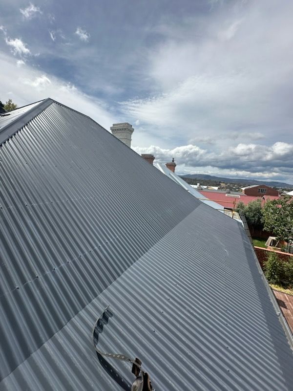 Corrugated metal roof under cloudy sky, with chimneys and houses in the distance