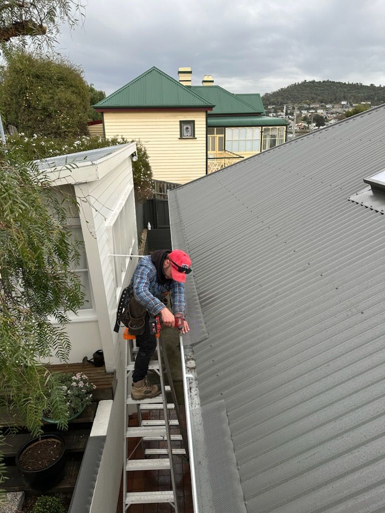 Person in red helmet descending a narrow ladder beside a sloped gray roof in an outdoor residential area