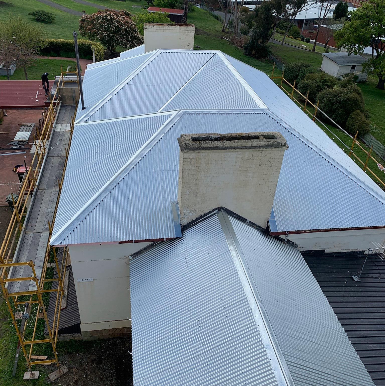Aerial view of a house with a newly installed silver metal roof and central chimney.