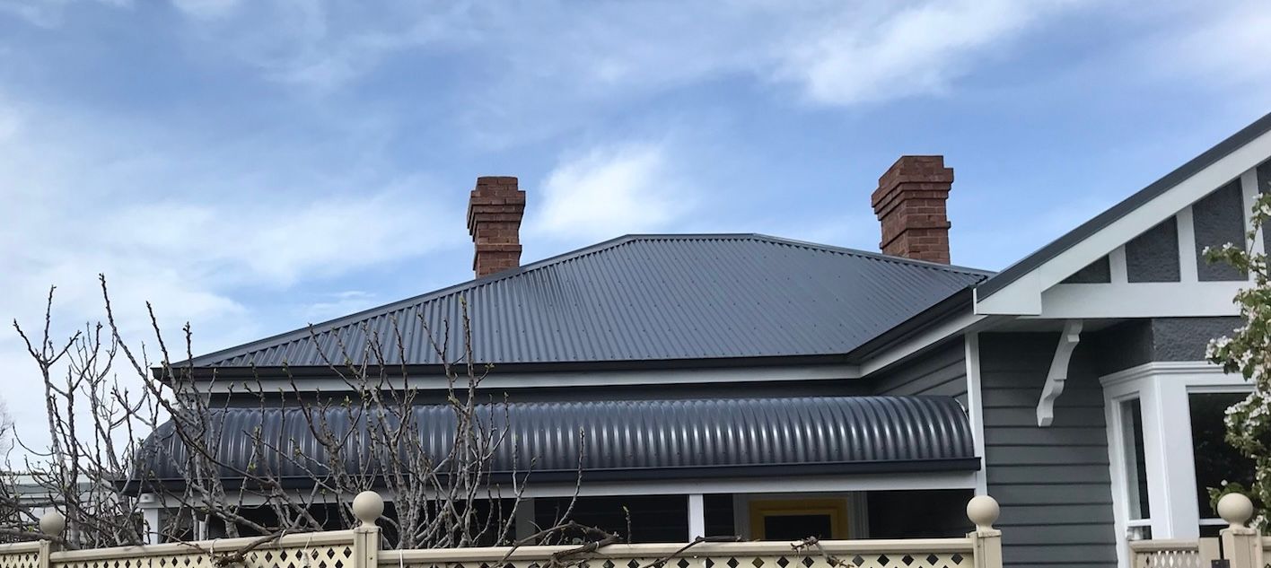 Blue-roofed house with two brick chimneys under a cloudy sky, framed by bare branches