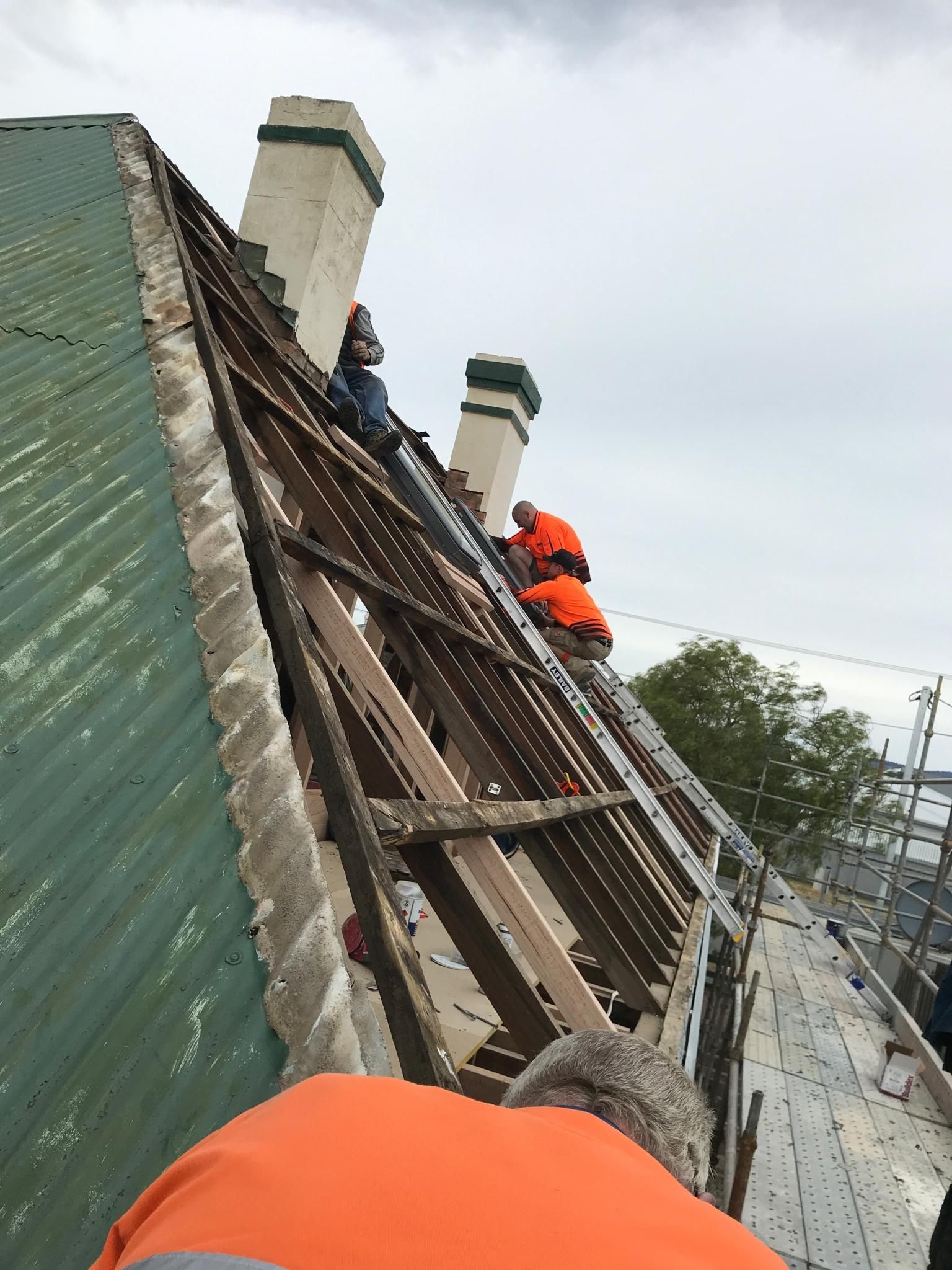 Workers climbing a steep roof with ladders and safety gear during roof repair