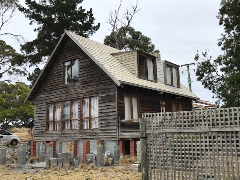 Weathered old wooden house with gray roof and lattice fence in a sparse yard