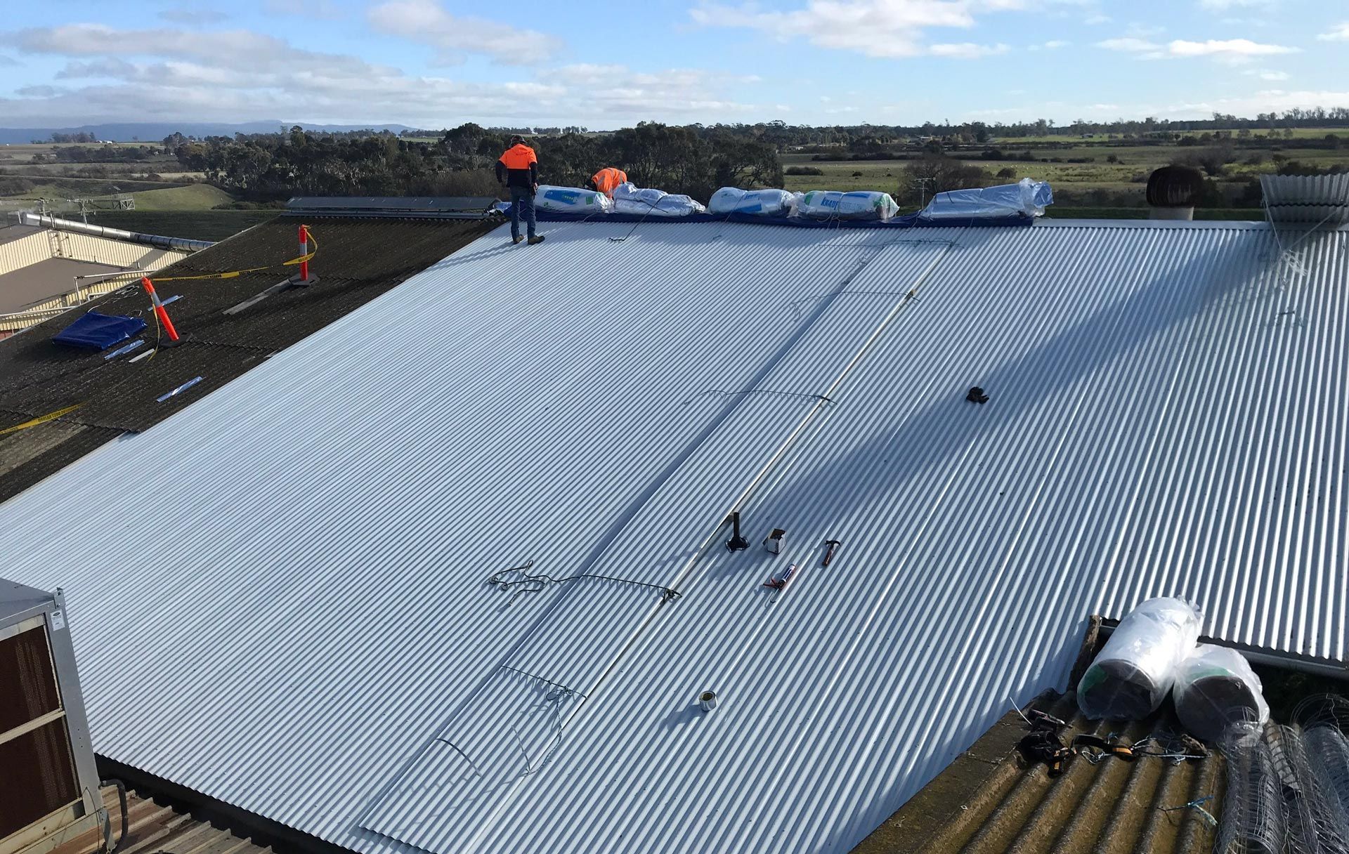 Roofers working on a large corrugated metal roof under a blue sky