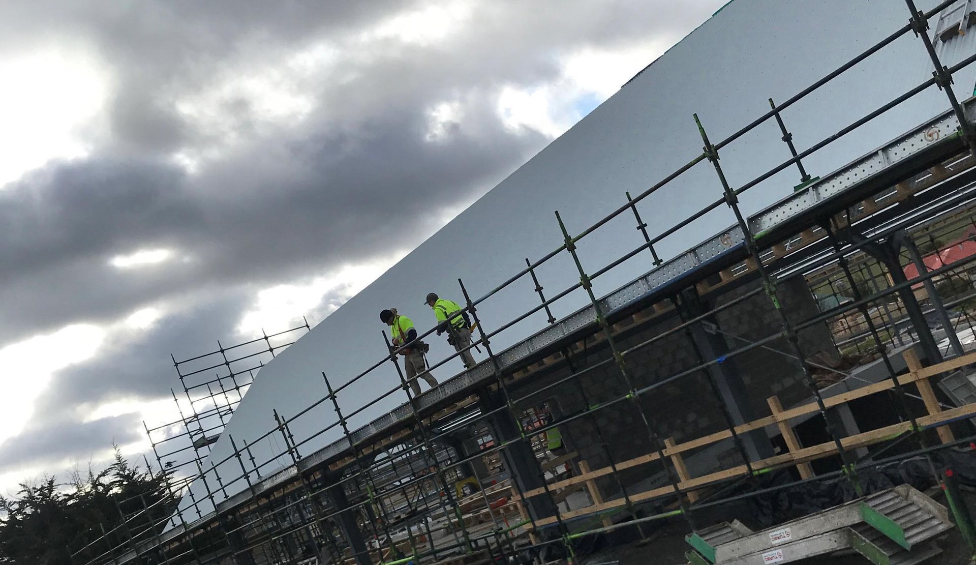 Workers in high-vis gear on scaffolding around a building under construction, beneath cloudy skies