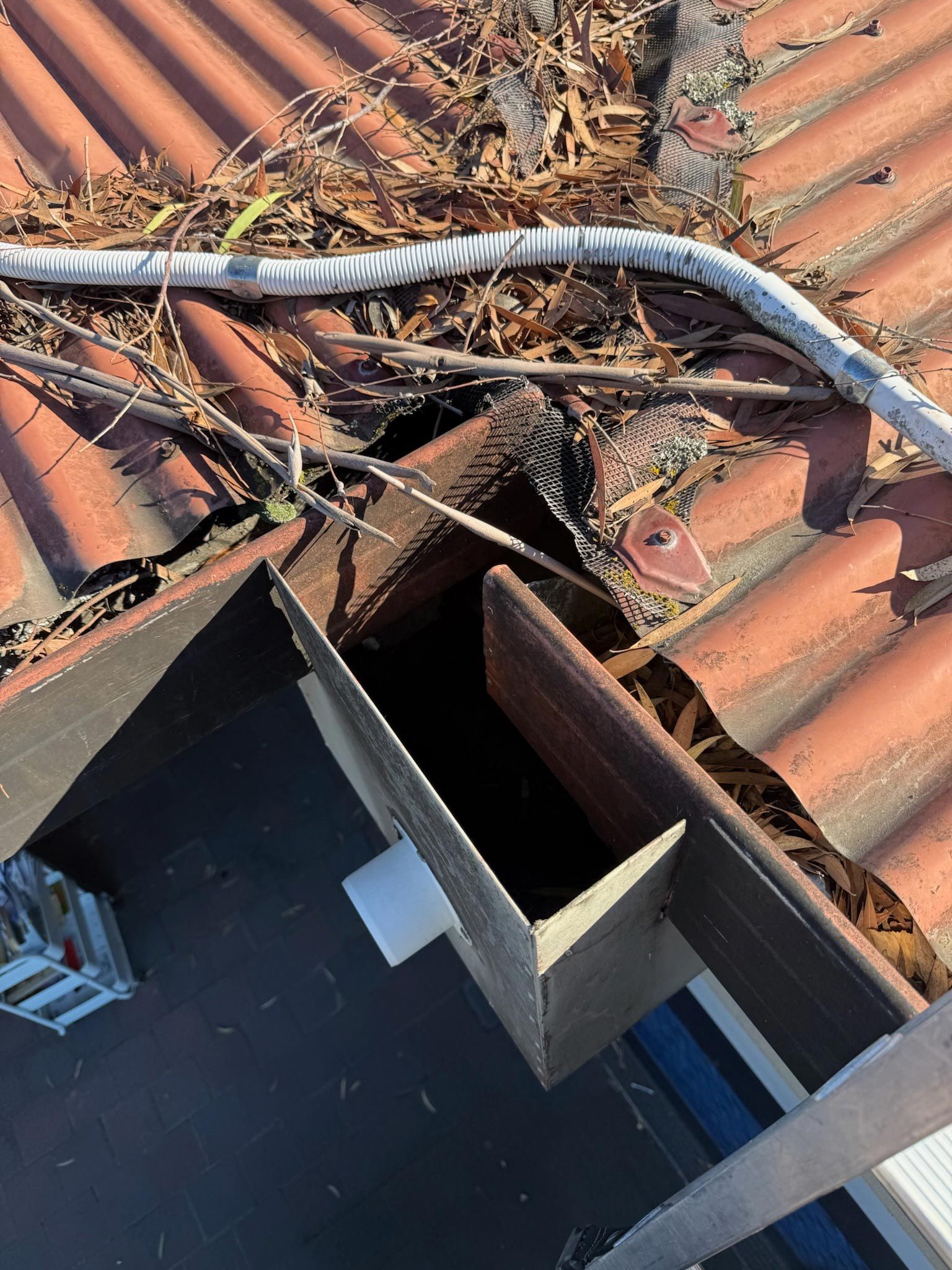 Damaged clay roof tiles with debris and exposed black roofing near a roof edge
