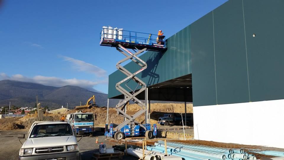 A worker on a blue scissor lift works on the wall of a large building under construction.