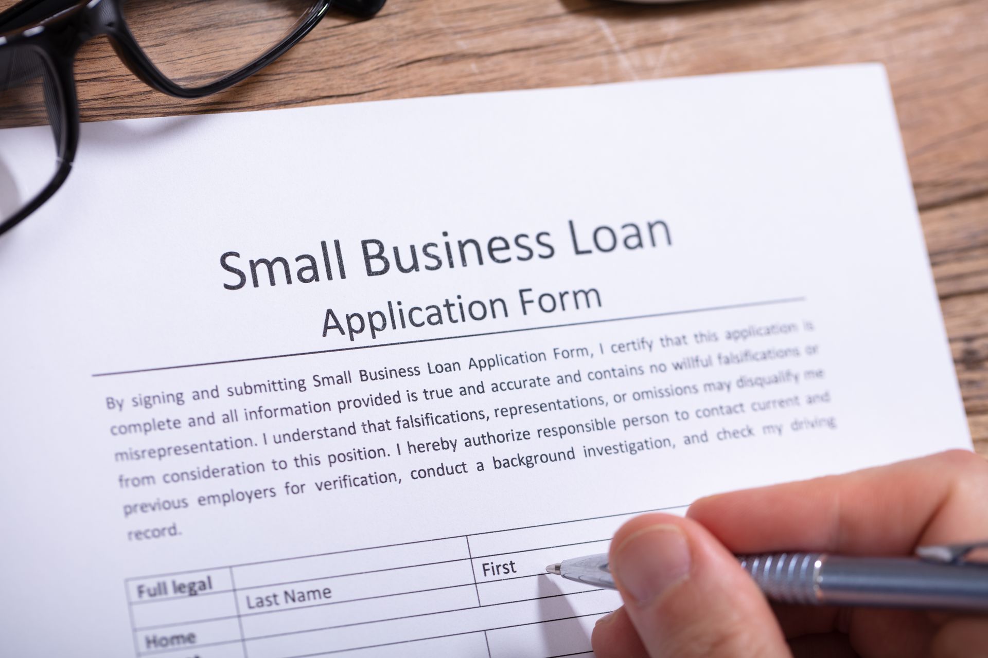 Person filling out a small business loan application form with a pen on a desk