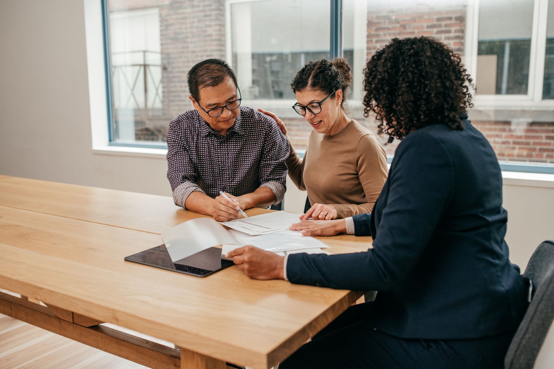 Three people reviewing documents at a wooden table in a bright office room