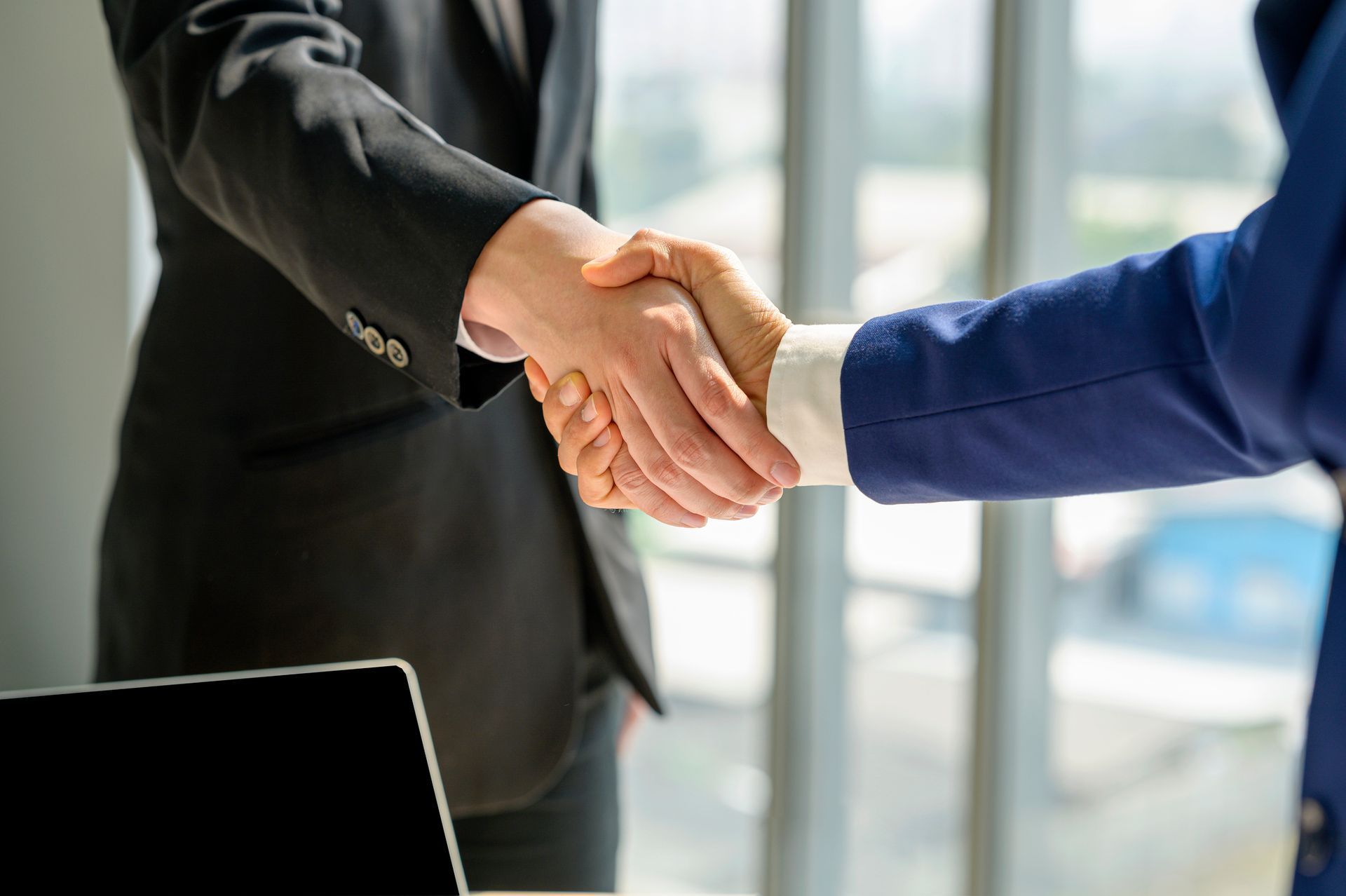 Two people in business attire shaking hands in an office setting.