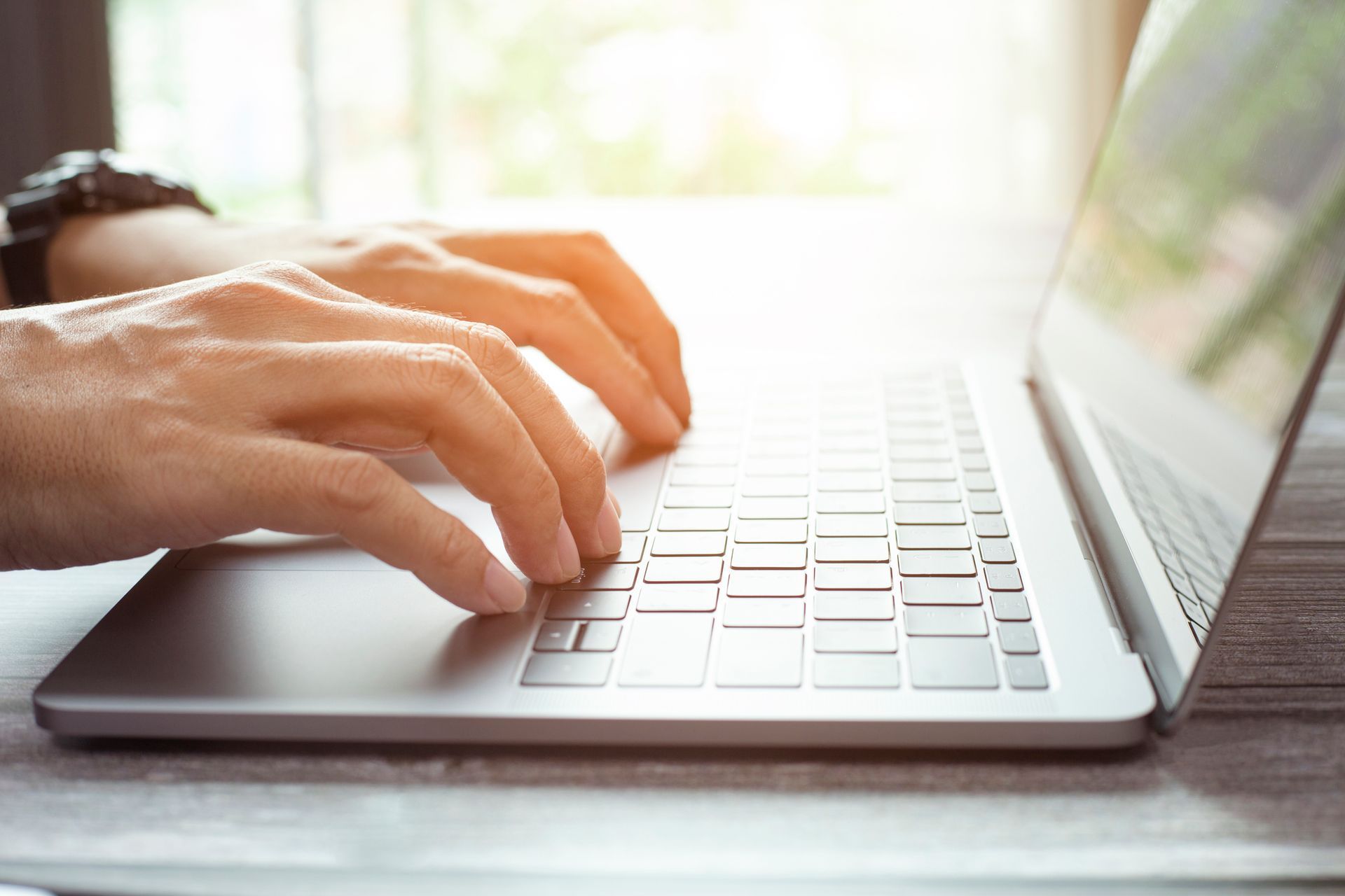 Hands typing on a silver laptop keyboard in bright natural light