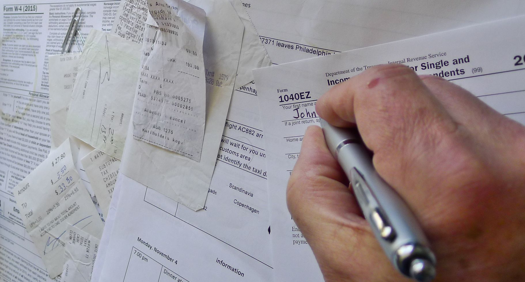Hand writing notes on scattered papers with a silver pen at a desk
