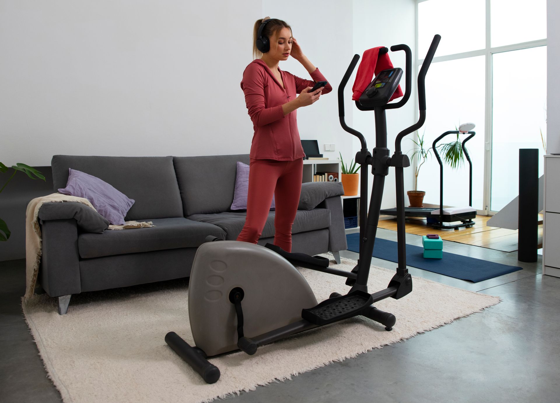 Person in red workout clothes using an elliptical machine in a living room with a sofa.
