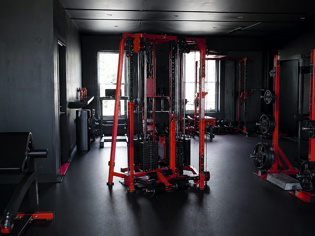 Two workers assembling a treadmill in a gym room, with tools and dumbbells nearby.