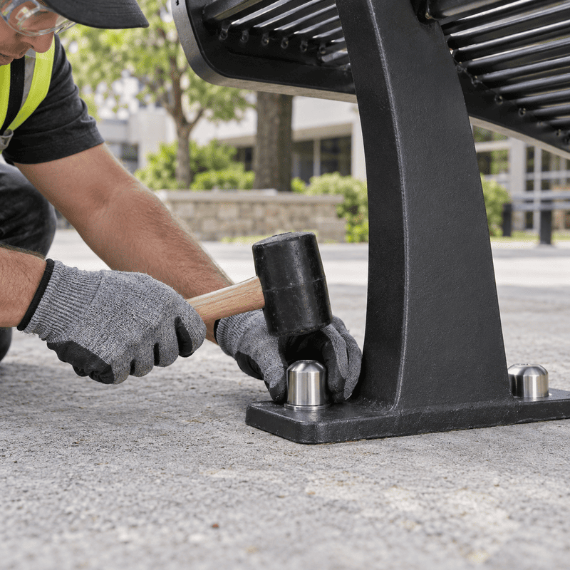 Worker using a mallet to secure a metal bench foot to concrete outdoors