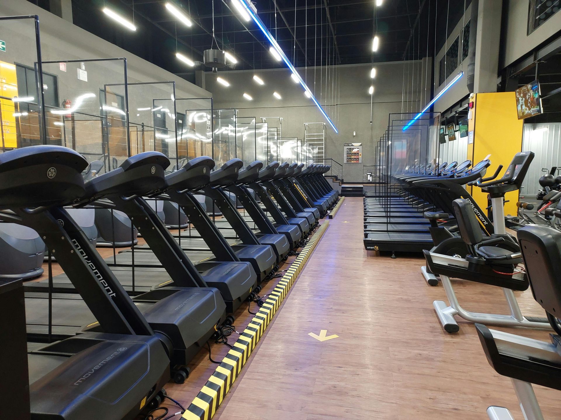 Row of treadmills in a modern gym with mirrored walls and bright overhead lights