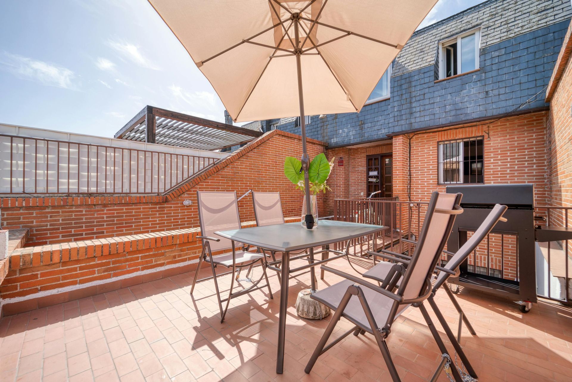 Sunlit rooftop patio with patio table, chairs, umbrella, and city view