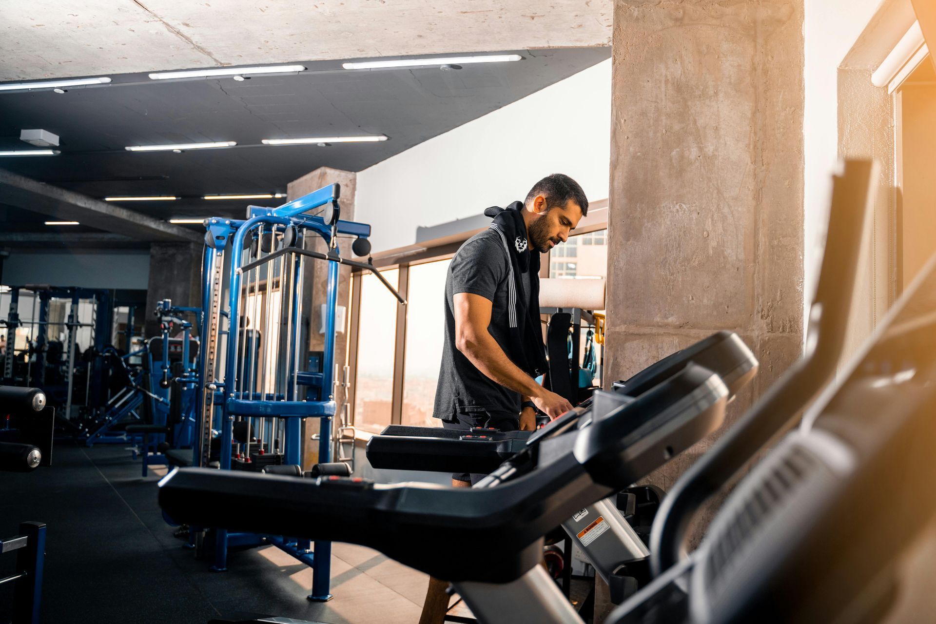 Man exercising on a treadmill in a gym with blue workout equipment and sunlight streaming in