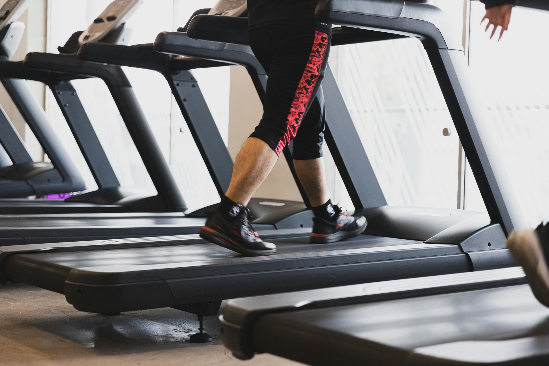 Person walking on a treadmill in a gym, wearing black leggings and sneakers.