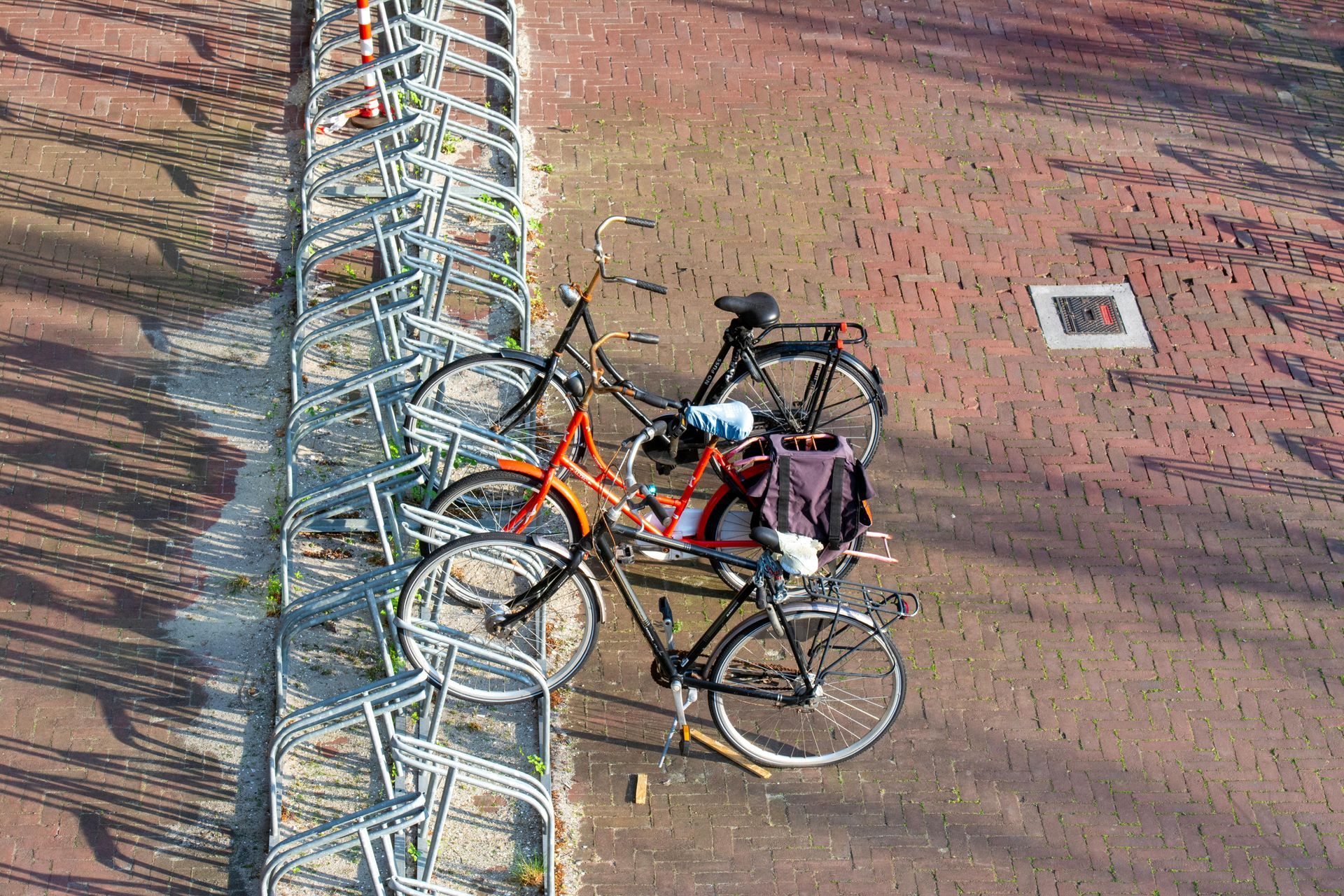 Bicycles locked to a metal rack on a brick-paved sidewalk, with one orange bike and one red bike visible