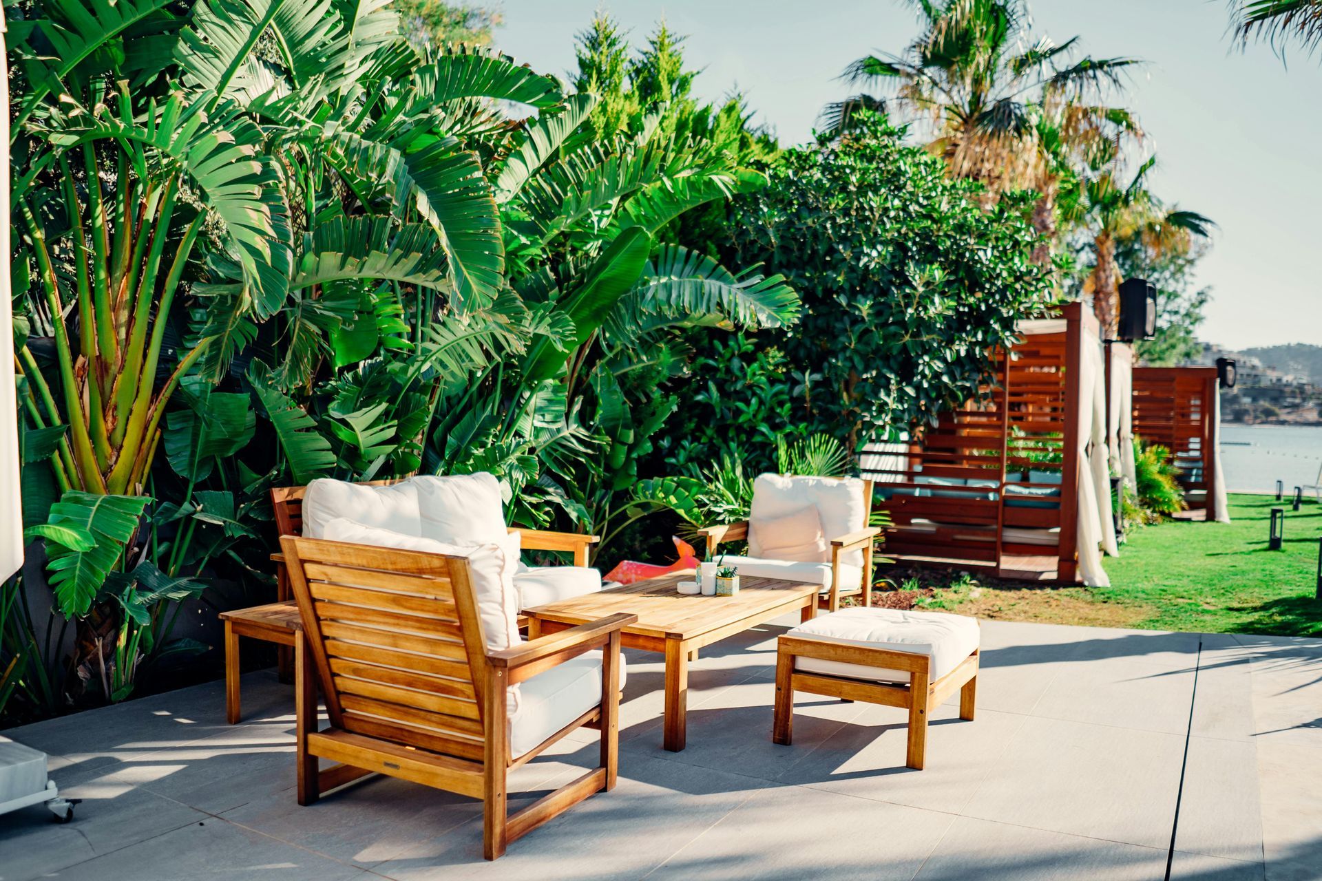 Patio seating with wooden chairs and a table beside lush tropical plants and a poolside deck