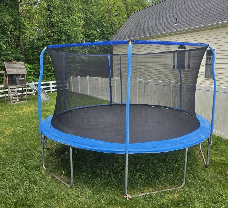 Blue and black trampoline in a grassy backyard with a safety net.