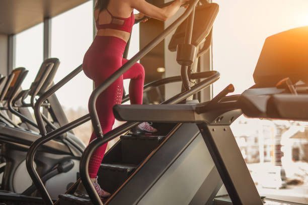 Person in a maroon workout set using a stair-climbing machine in a gym near a window during sunset.