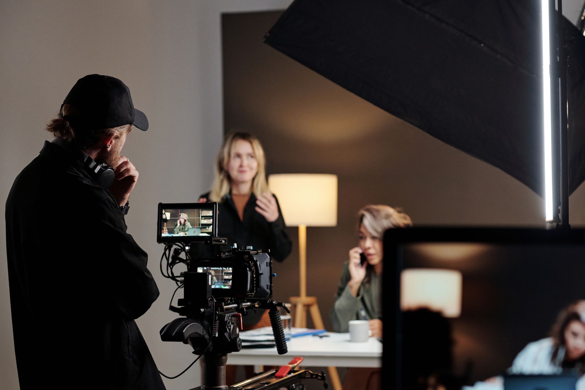 Back view of young videographer standing in front of steadicam during shooting of commercial with female model in studio - using video branding to increase brand awareness