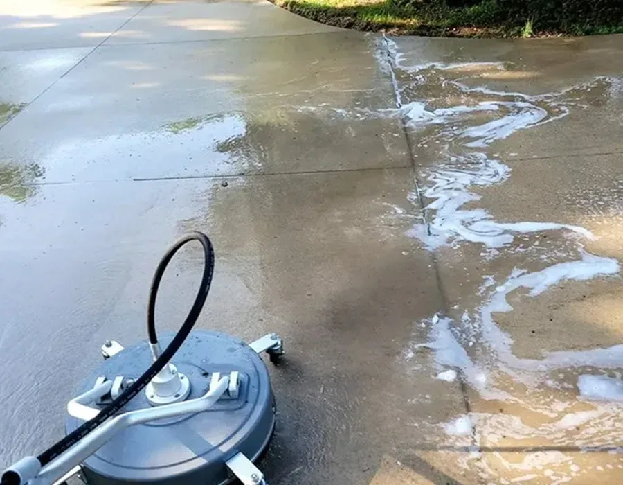 Pressure washer cleaning a wet concrete driveway with soap suds.