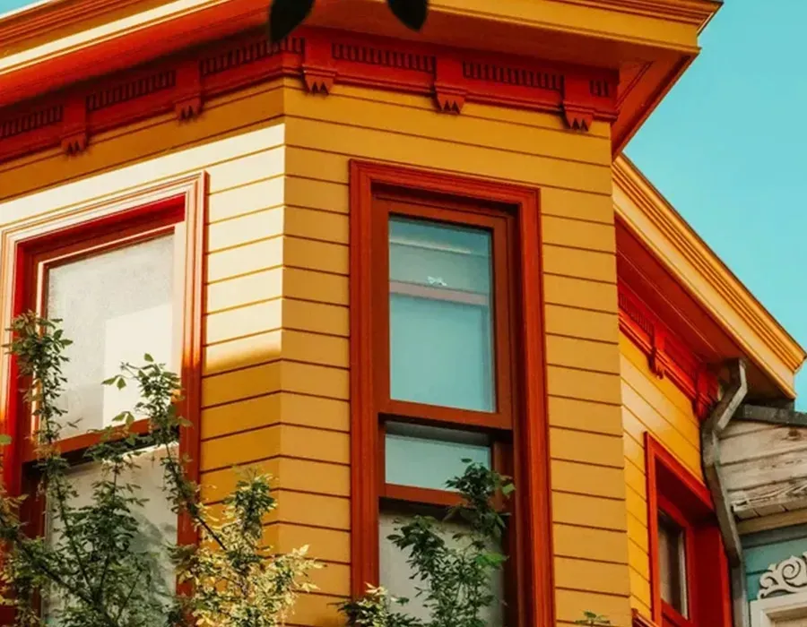 Colorful orange and yellow building corner with red-trimmed windows against a blue sky